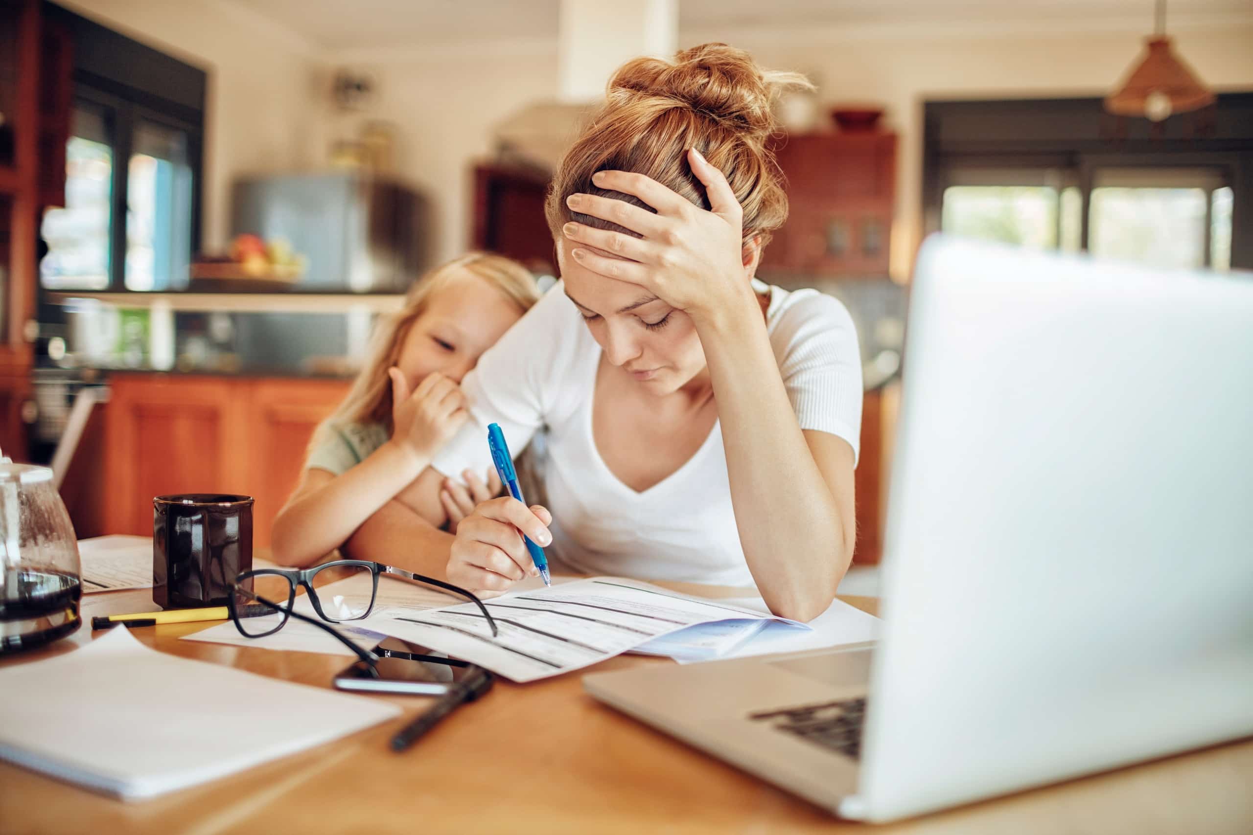 young girl comforting her mother during a financial crisis at home while adult looks at papers near a lap top