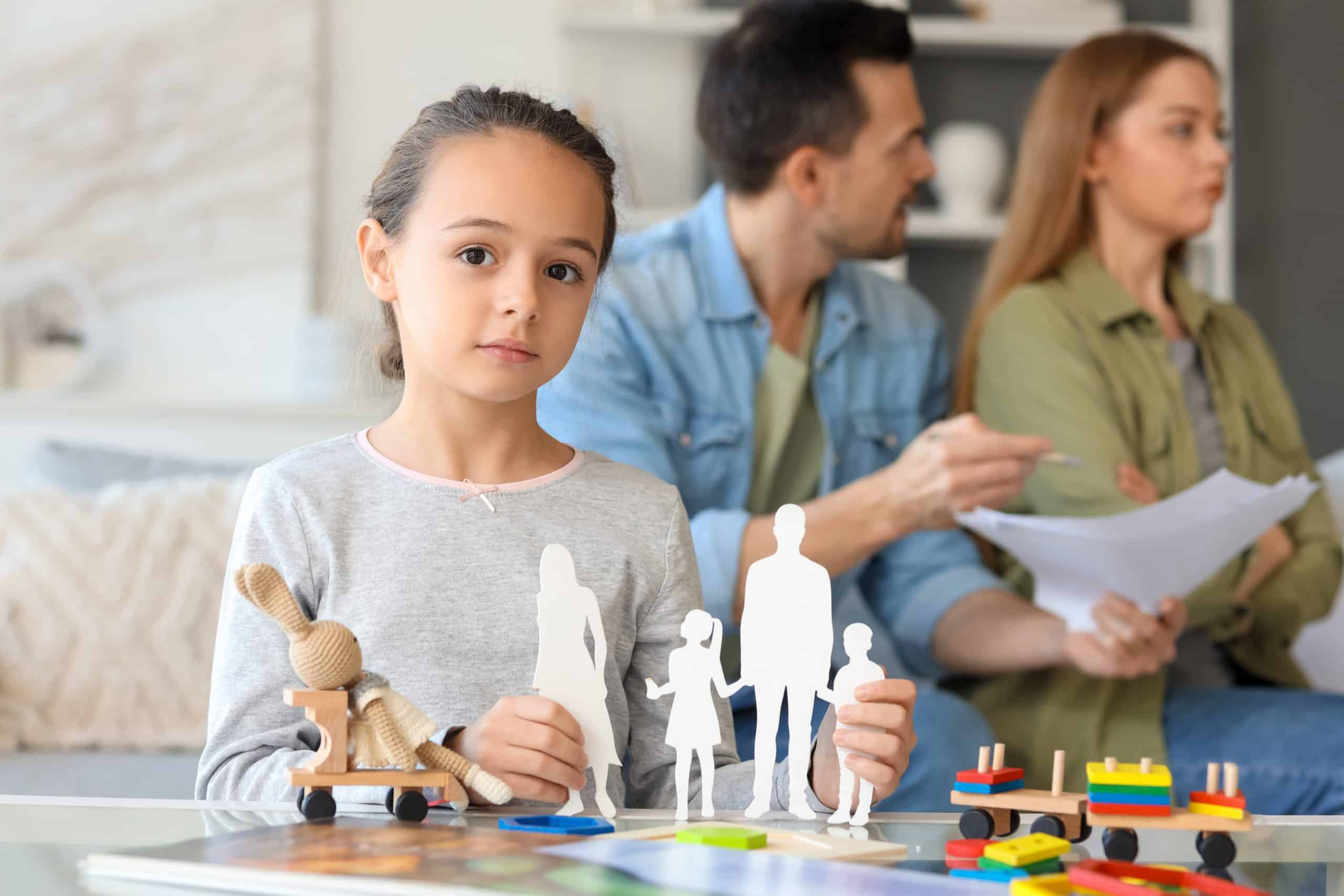 Sad youong girl playing with toy family figure and her parents getting divorce at home